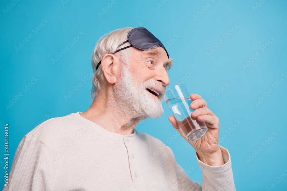 Profile side photo of aged man pensioner drink water happy smile wear pajamas look empty space isolated over blue color background Profile side photo of aged man pensioner drink water happy smile wear pajamas look empty space isolated over blue color background