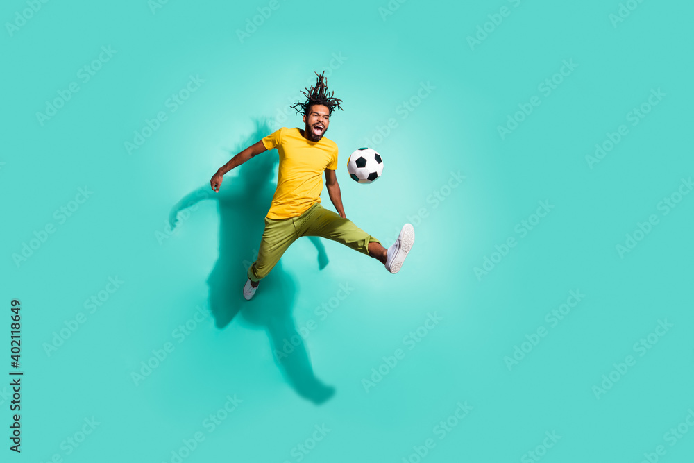 Full size photo of young smiling positive happy afro man jumping playing football isolated on teal color background