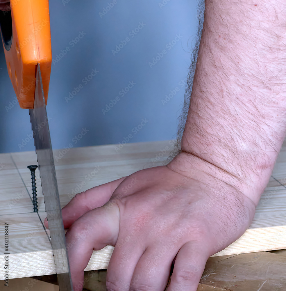 A carpenter saws a wooden board on a small wooden stool