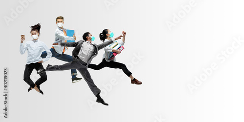 Happy office workers in face masks jumping and dancing in casual clothes or suit isolated on studio background. Business  start-up  prevention of COVID  motion and action concept. Creative collage.