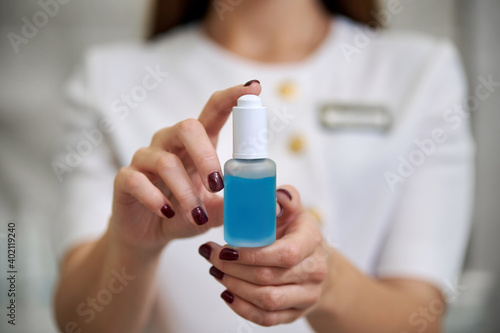 Selective focus of a bottle with serum for face treatment. A beautiful brunette holding a transparent bottle with serum for face treatment