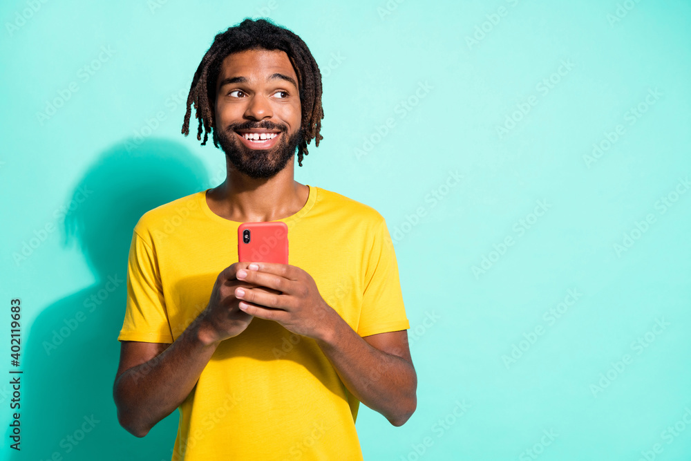 Photo portrait of dreamy afro american guy looking at blank space holding phone in two hands isolated on vivid cyan colored background Photo portrait of dreamy afro american guy looking at blank space holding phone in two hands isolated on vivid cyan colored background