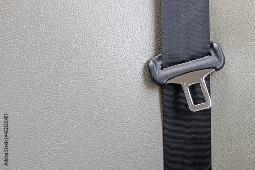 Buckle and strap of a car seatbelt against a pale cream blank leather background