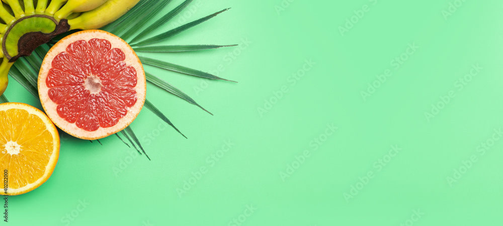 Tropical fruits summer banner background. Bananas, oranges and grapefruits on a colored green background. Smoothie, summer vacation, sun and vitamins concept. Tropical fruits summer banner background. Bananas, oranges and grapefruits on a colored green background. Smoothie, summer vacation, sun and vitamins concept.