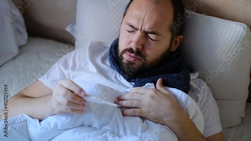 The man is sick in bed, checking the temperature. A person having a high fever watching a thermometer. The man is sick at home.