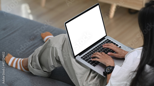 A young woman freelancer working on laptop computer while sitting on sofa in living room.