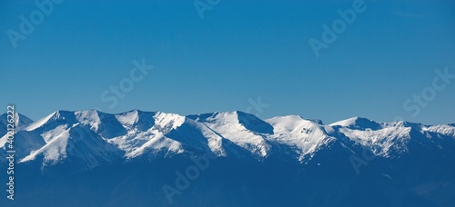 Beautiful winter panoramic mountain landscape. The white snowy peaks of Pirin Mountains, viewed from The Rila Mountains in Bulgaria, blue sky. Snowy weather conditions for winter sports and tourism.