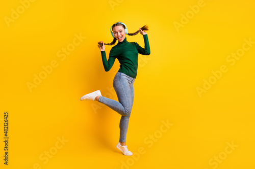 Full length body size view of pretty cheerful girl listening music jumping dancing isolated on bright yellow color background photo