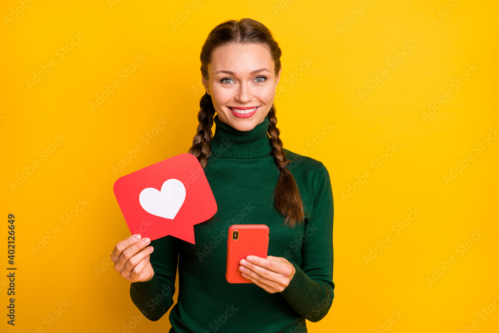Photo portrait happy woman with braids showing heart icon keeping mobile phone isolated vivid yellow color background Photo portrait happy woman with braids showing heart icon keeping mobile phone isolated vivid yellow color background
