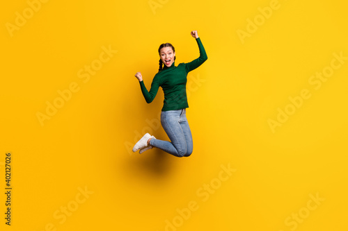 Full length body size photo smiling woman jumping high gesturing like winner isolated on bright yellow color background © deagreez