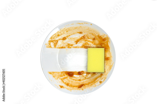 Obraz na plátně White round dirty plate with red sauce, yellow foam sponge cleaning dish top view , isolated on white background