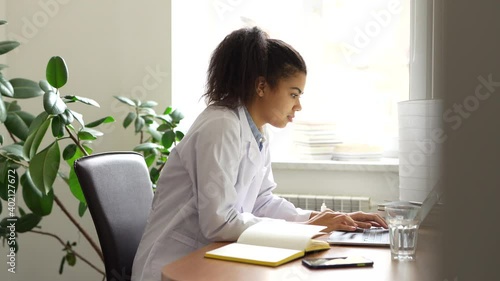 Internship. Enthusiastic young female medical student typing while studying using her laptop indoors. Health, medicine, online education and technology. Side view