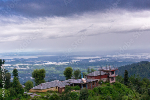 building perched on the edge of a mountain with trees all around looking over a beautiful vista landscape of a valley covered in clouds at dawn shot in Mcleodganj of dharamshala 