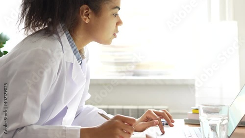 Knowledge. Close up of young mixed race girl, medical student making notes while studying using her laptop computer. Health, medicine, education and technology. Side view