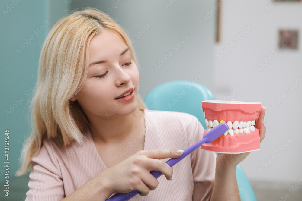Lovely woman showing how to brush teeth correctly, holding jaw model and toothbrush Lovely woman showing how to brush teeth correctly, holding jaw model and toothbrush