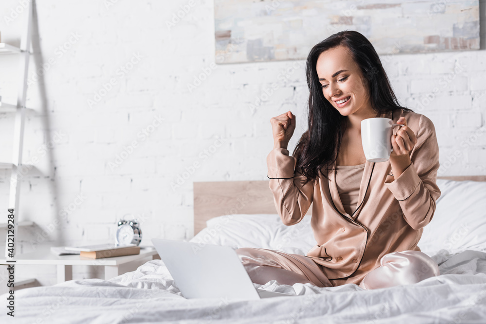 happy brunette woman sitting in bed with mug and laptop at morning happy brunette woman sitting in bed with mug and laptop at morning