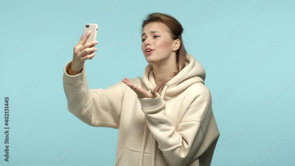 Slow motion of beautiful girlfriend video chat with boyfriend and telling she love and miss him, looking at smartphone front camera during call, standing over blue background Slow motion of beautiful girlfriend video chat with boyfriend and telling she love and miss him, looking at smartphone front camera during call, standing over blue background