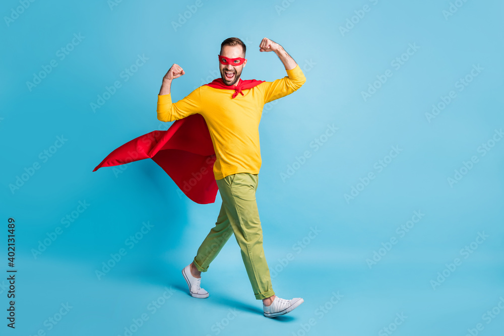 Full size photo of young handsome powerful superhero go walk showing muscles biceps isolated on blue color background Full size photo of young handsome powerful superhero go walk showing muscles biceps isolated on blue color background
