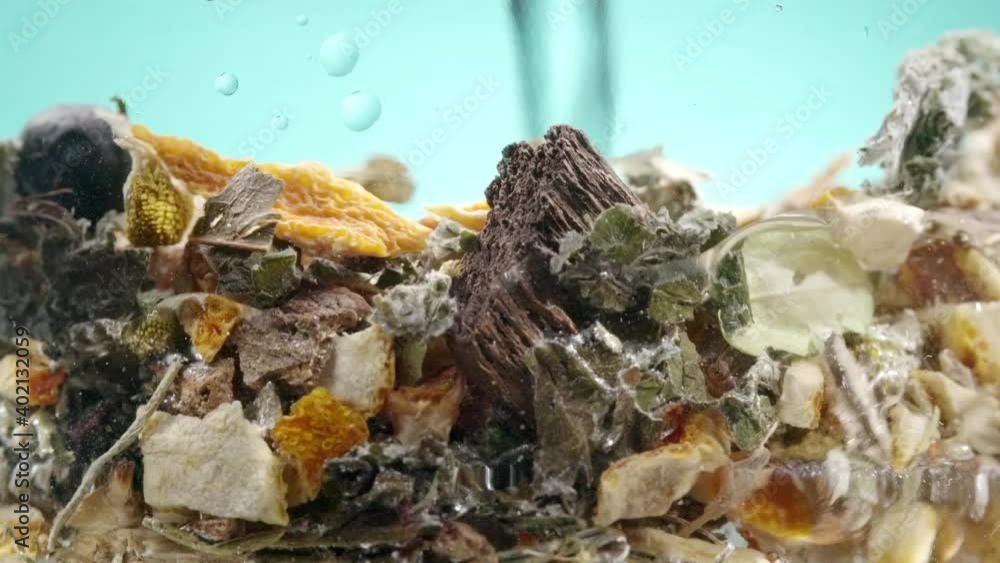 Water pouring in glass with lots of fruits, herbs and spices. Tea brewing, beverage making. Healthy natural drink closeup on cyan background Water pouring in glass with lots of fruits, herbs and spices. Tea brewing, beverage making. Healthy natural drink closeup on cyan background