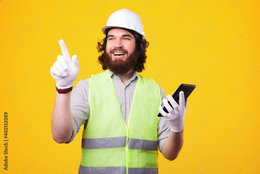 Handsome young architect man holding tablet and pointing away over yellow background. Handsome young architect man holding tablet and pointing away over yellow background.