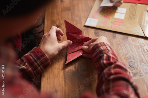 Unrecognizable woman wearing red checked shirt using colored paper to make origami crane, high angle medium close-up shot