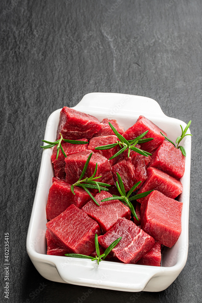 Cubes of raw beef meat on black stone background