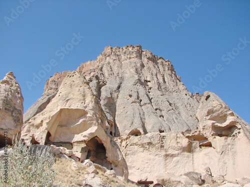 Panorama from the bottom of impregnable rocks on a background of sunny blue sky under the rays of the midday sun.