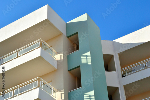 Modern White Apartment Building with Balconies seen from Below against Blue Sky