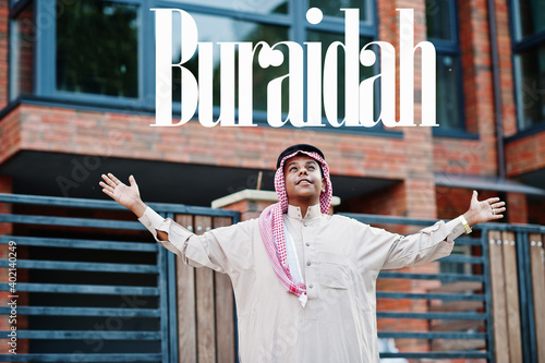 Buraidah - biggest city of Saudi Arabia. Middle Eastern saudi arabian man posed on street against modern building up his hands in the air. photo