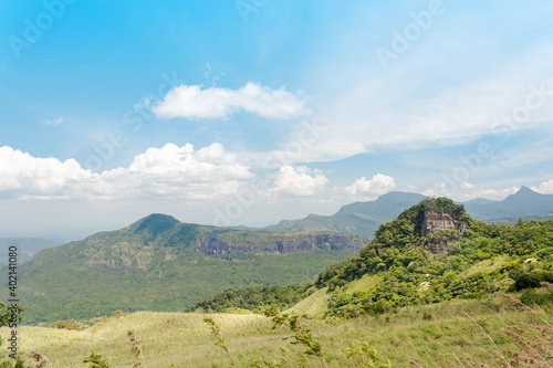 Single rock peak covered by trees and bushes with a background mountain range.