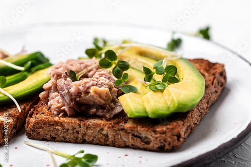 toasts, sandwiches with canned tuna and avocado on a white plate on a light background. Long banner format, top view