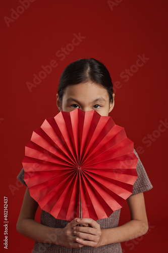 Unrecognizable Asian girl standing against red wall background holding traditional Chinese paper fan looking camera © Seventyfour