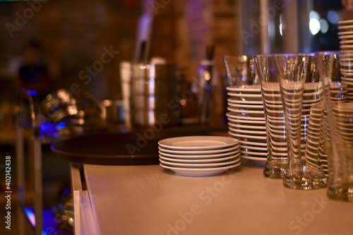 Stacks of clean dishes on the table of the bollard. White ceramic plates and saucers, glass transparent glasses.