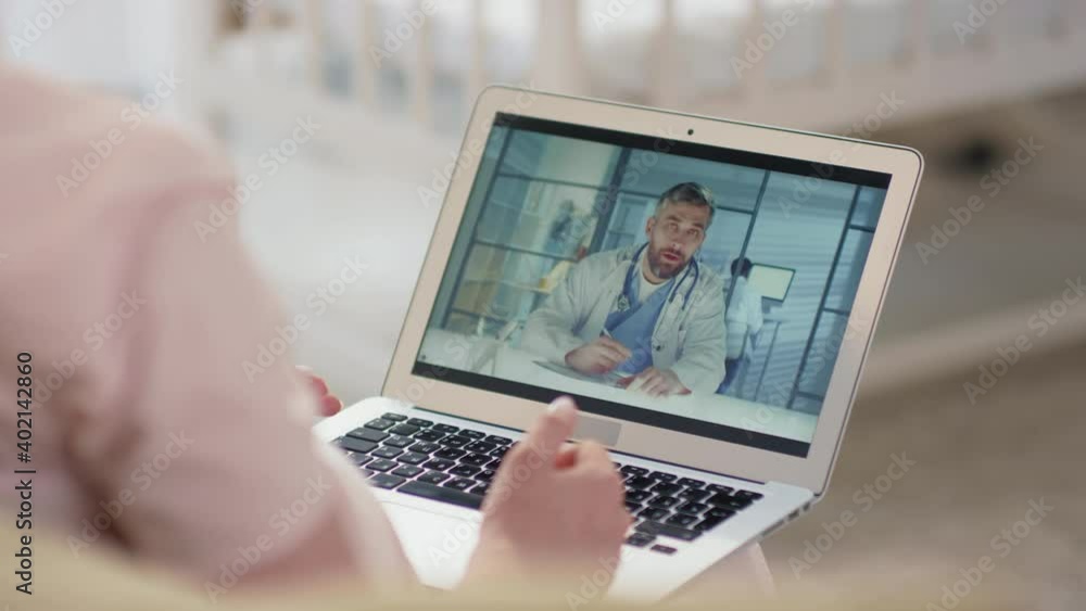 Over-the-shoulder close-up of unrecognizable pregnant woman sitting at home having online video conversation with male obstetrician-gynecologist via laptop Over-the-shoulder close-up of unrecognizable pregnant woman sitting at home having online video conversation with male obstetrician-gynecologist via laptop