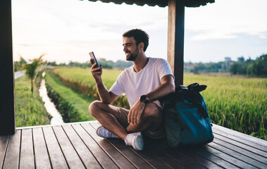 Cheerful male traveler using cellphone in tropical countryside