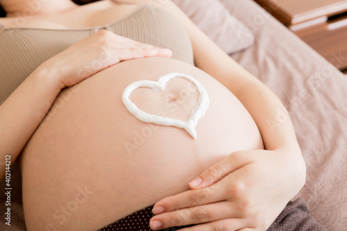 Wallpaper Mural a pregnant girl sits at home on the bed and smears heart an anti-stretch mark cream on her stomach. Pregnancy, motherhood, preparation and expectation concept Torontodigital.ca