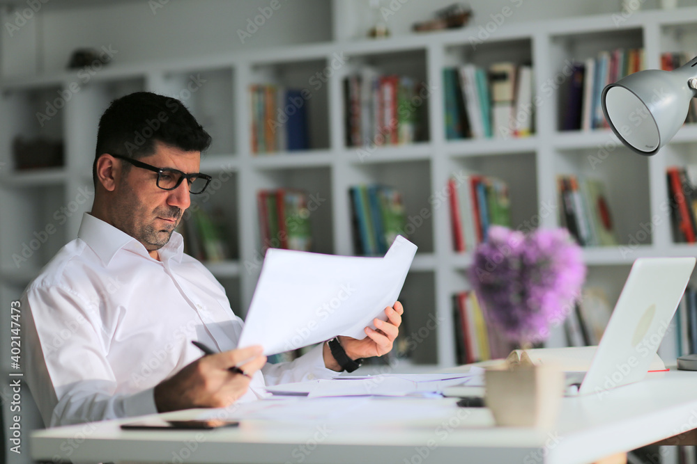 Young businessman sitting at a table at home working on a laptop and writing down ideas in a notebook Young businessman sitting at a table at home working on a laptop and writing down ideas in a notebook