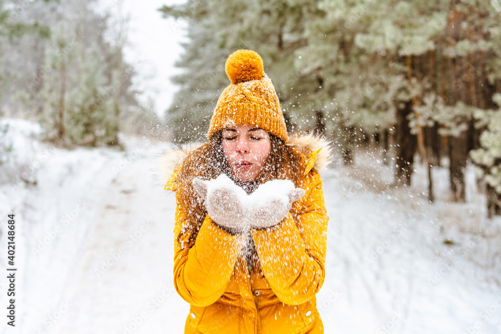 Beautiful young woman in yellow jacket and hat throws snow in snowy winter forest Beautiful young woman in yellow jacket and hat throws snow in snowy winter forest