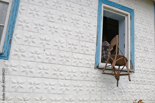 Fototapeta Naklejka Na Ścianę i Meble -  A man throws an old chair out of the window