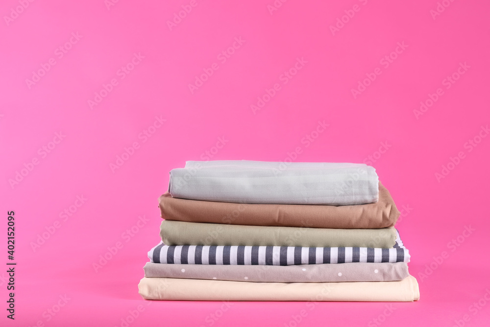 Stack of clean bed sheets on pink background. Space for text Stack of clean bed sheets on pink background. Space for text