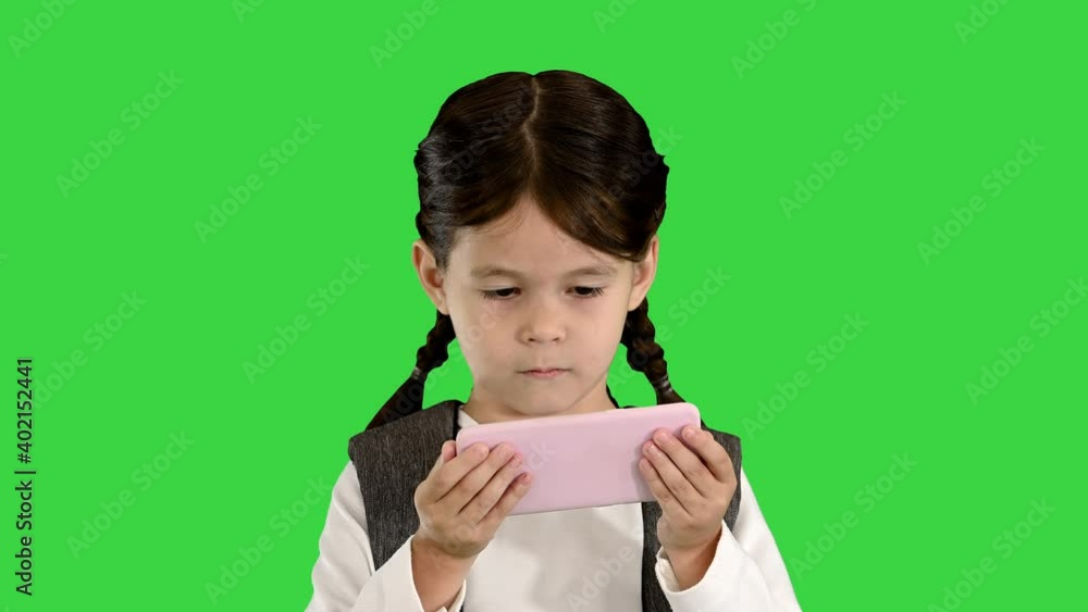 School girl with backpack watching something on her pink phone on a Green Screen, Chroma Key. School girl with backpack watching something on her pink phone on a Green Screen, Chroma Key.