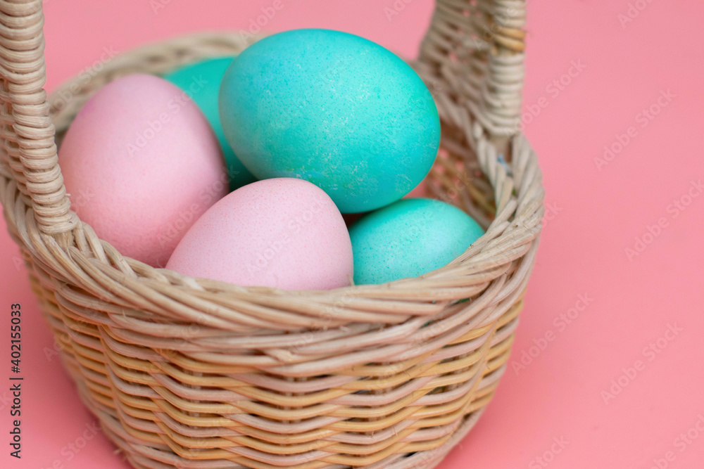 Easter decor: colored eggs in a basket, pink background, pastel colors, close-up. Preparing for Easter. The photo