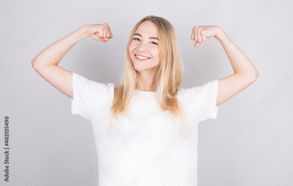 © MP Studio - Young pretty blonde woman feeling happy, satisfied and powerful, flexing fit and muscular biceps, looking strong after the gym against white wall