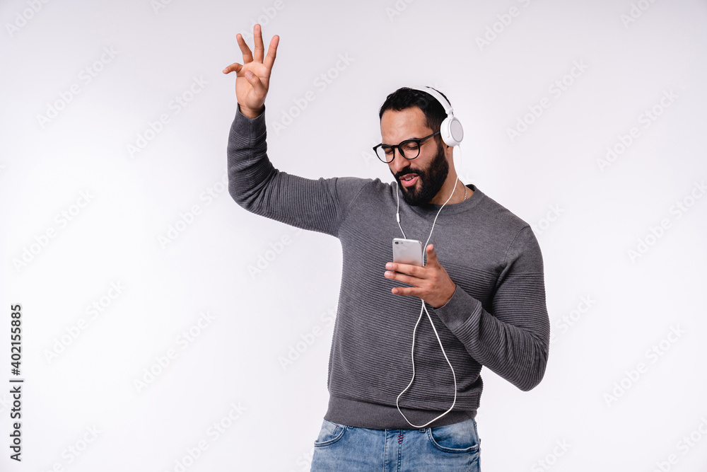 Fototapeta premium Handsome Arabian young boy listening to the music and dancing in headphones isolated over white background