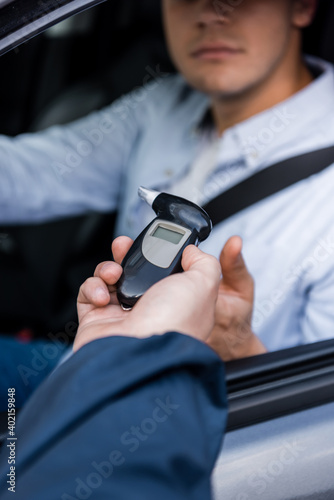 Obraz na plátně cropped view of policeman giving breathalyzer to driver sitting in car on blurred background