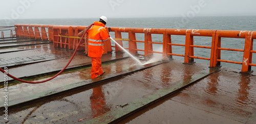 a sailor washes the deck of a ship with the pressure of sea water from a fire hose