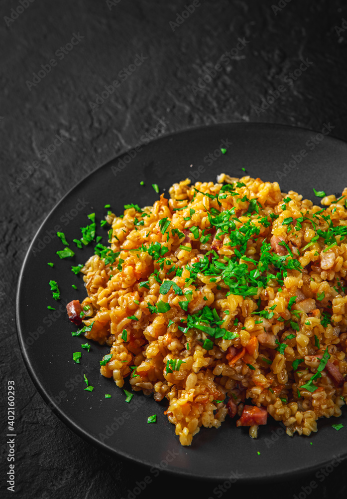 Bulgur with vegetables and meat on black plate on Dark grey black slate background Bulgur with vegetables and meat on black plate on Dark grey black slate background