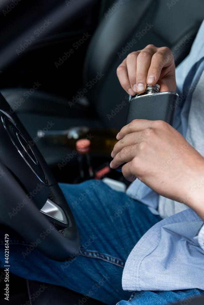 cropped view of man opening flask with alcohol while sitting in car at drivers seat.