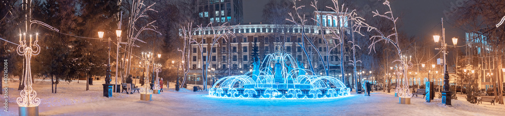 Wide panoramic view of the illuminated with garlands and twinkling lights fountain in the center of Ufa, Russia. Christmas and New Year decorations and holidays.