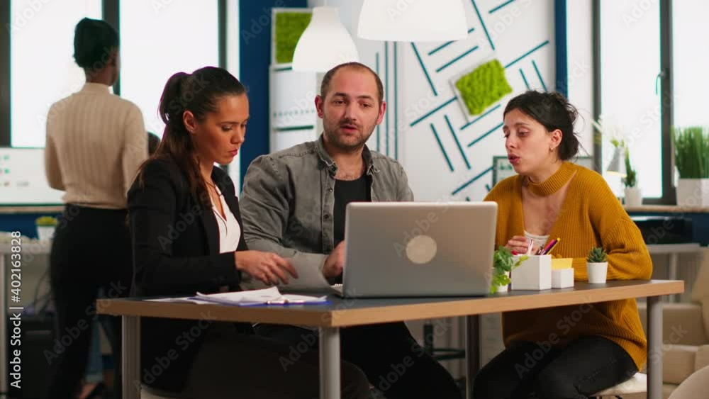 Enthusiastic concentrated business colleagues discussing holding documents and charts, analyzing company financial reports using laptop while multicultural team working together in modern office. Enthusiastic concentrated business colleagues discussing holding documents and charts, analyzing company financial reports using laptop while multicultural team working together in modern office.